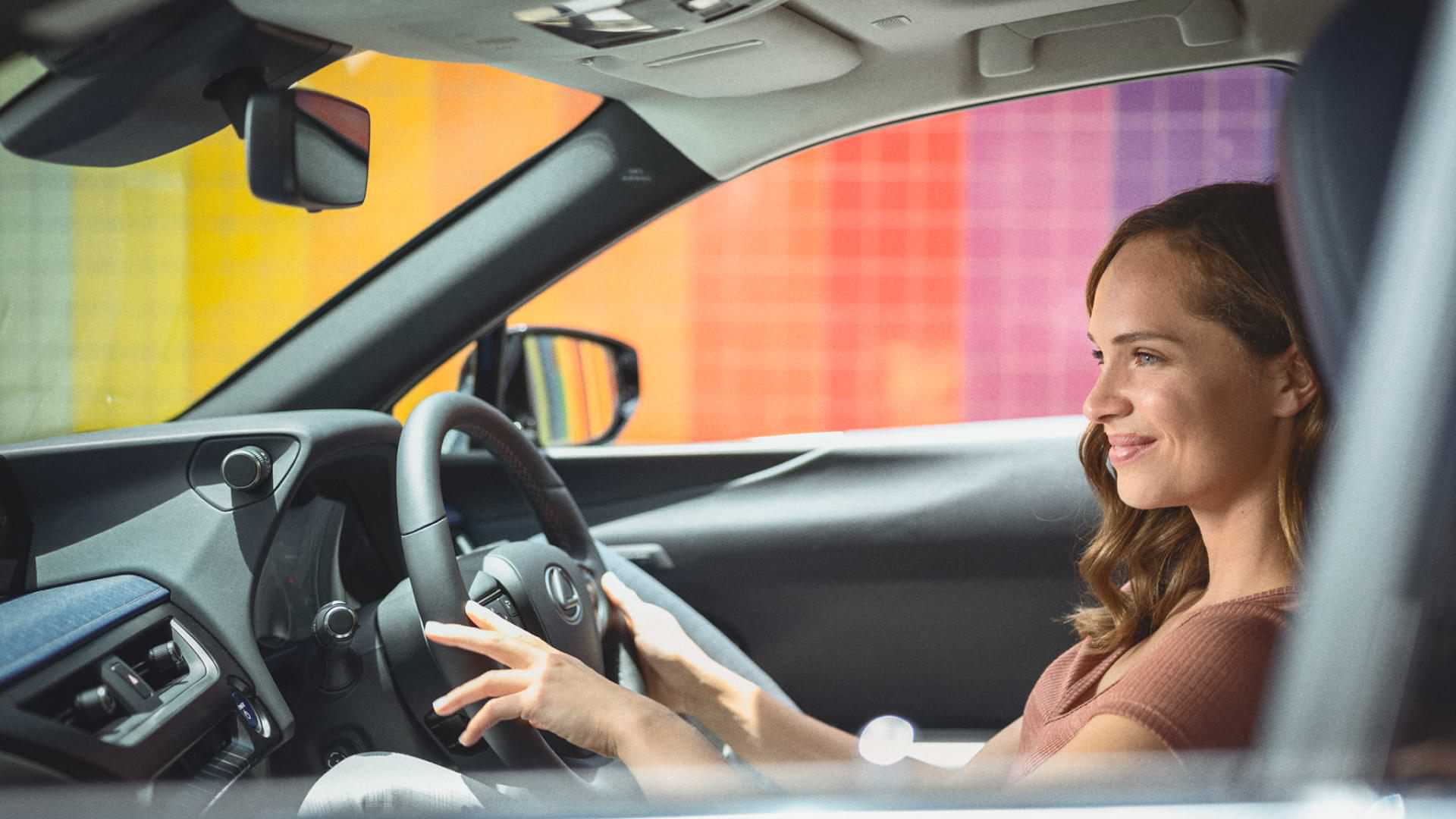 A woman drives a 2021 UX, a rainbow coloured wall is the background.
